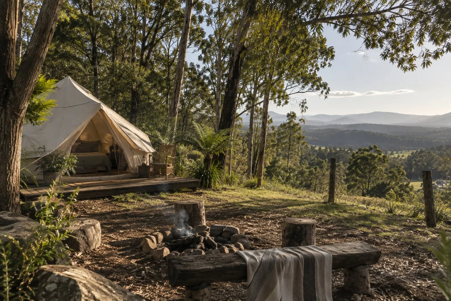 A canvas bell tent on a timber deck among gum trees, with a fire pit and views over the valley